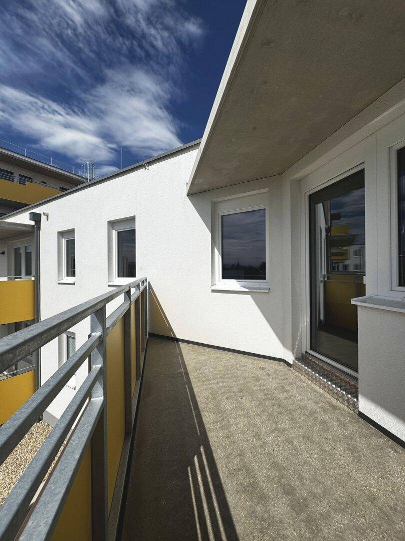 Langer Balkon mit gelben Akzenten und Blick auf die umliegende Bebauung unter klarem Himmel.