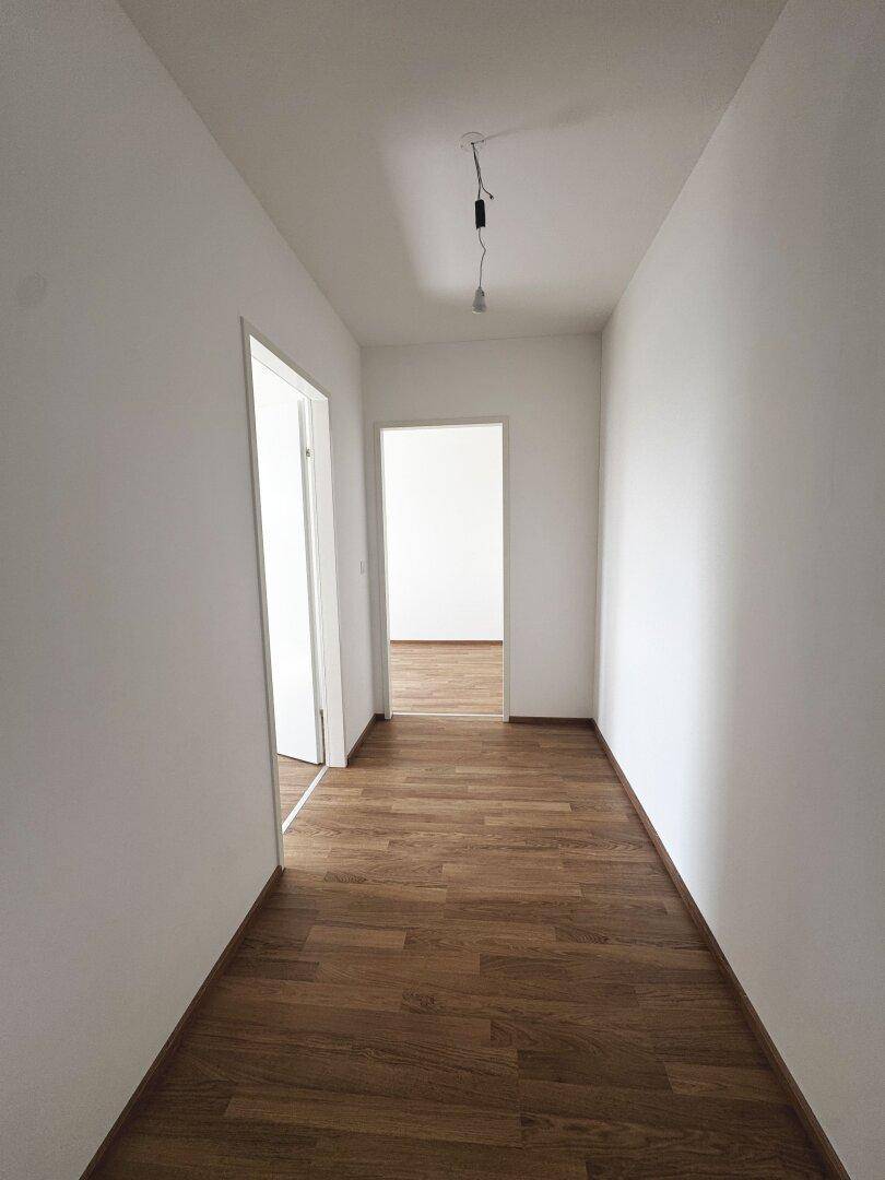 Langer, heller Flur mit Laminatboden und weißen Wänden, der die Räume verbindet.