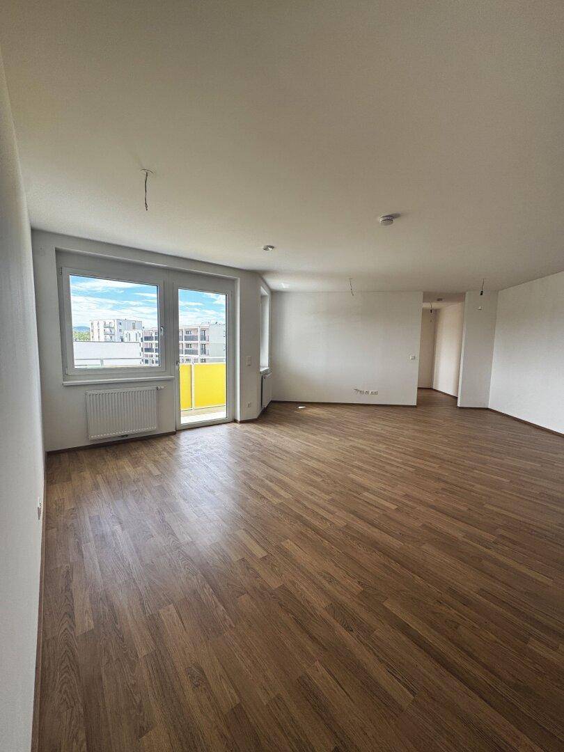 Geräumiger, heller Wohnbereich mit Laminatboden und Fensterfront zum Balkon.