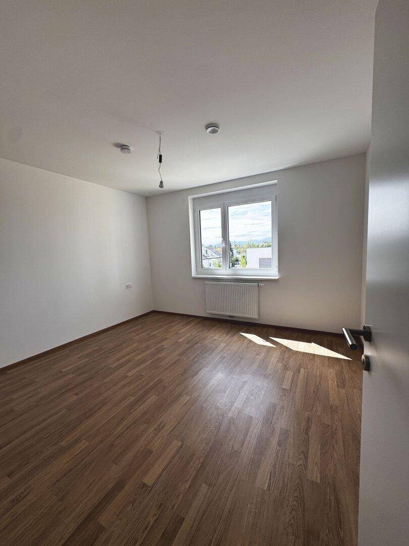Helles Schlafzimmer mit Laminatboden und einem Fenster, das viel Tageslicht hereinlässt.