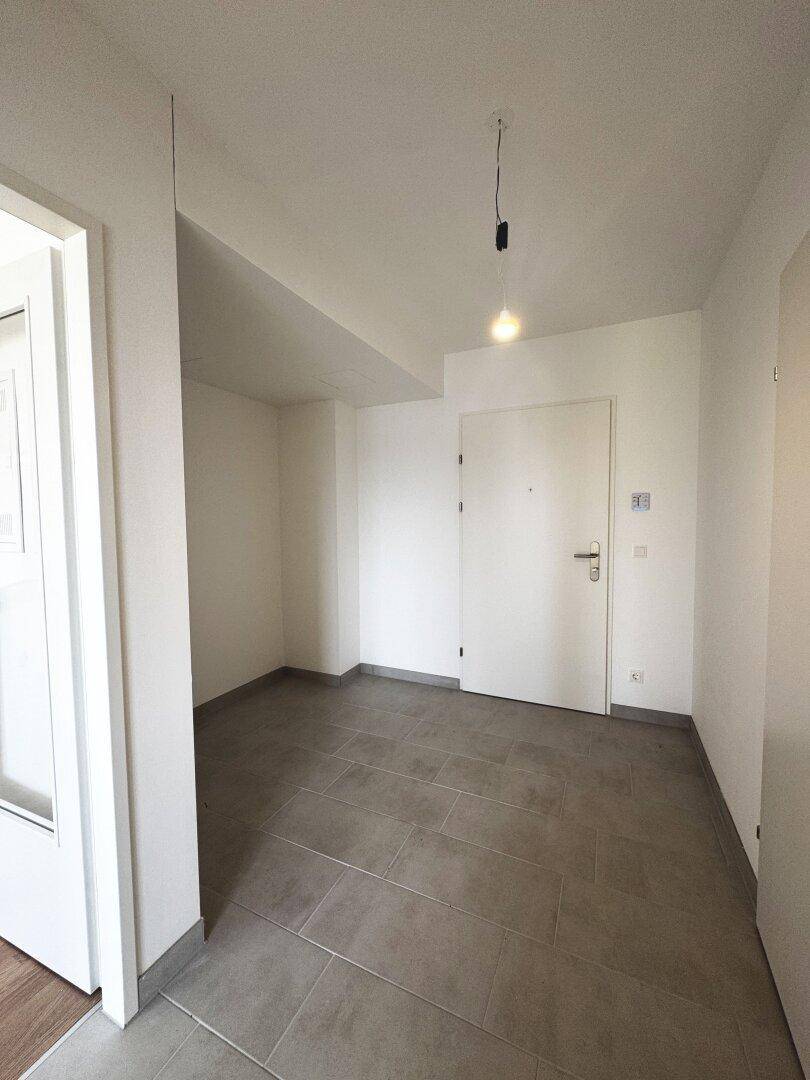 Geräumiger Eingangsbereich mit grauen Fliesen und der modernen Wohnungseingangstür.