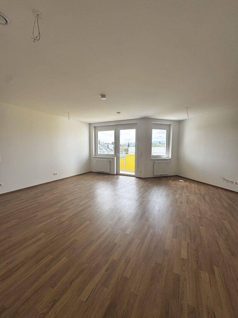 Heller Wohnraum mit Laminatboden und großen Fenstern, die Zugang zu einem Balkon bieten.