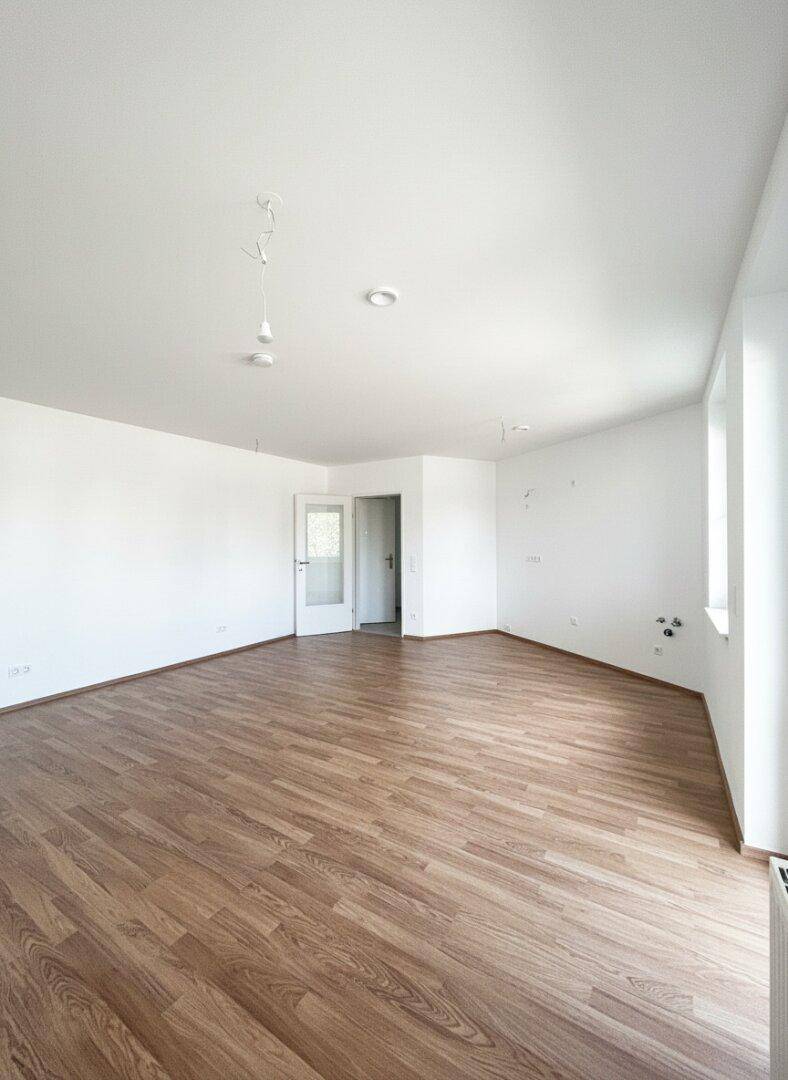 Geräumiges, leeres Zimmer mit hellem Laminatboden und weißen Wänden, bereit zur Einrichtung.
