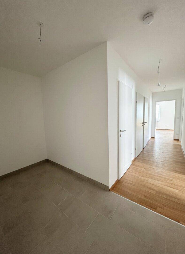 Geräumiger Flur mit modernem Fliesenboden, der in einen Bereich mit Laminat übergeht.
