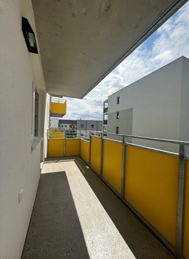 Heller Balkon mit gelben Sichtschutzwänden und Blick auf die umliegenden Neubauten.