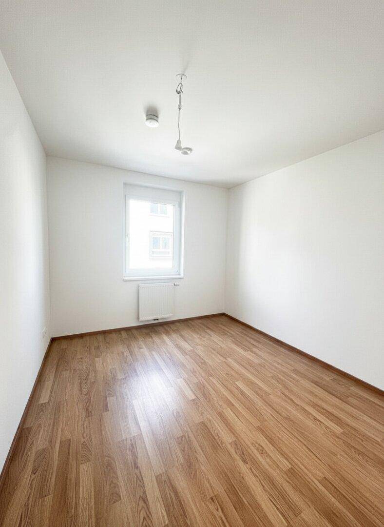 Helles Schlafzimmer mit Laminatboden und einem Fenster, das viel Tageslicht hereinlässt.