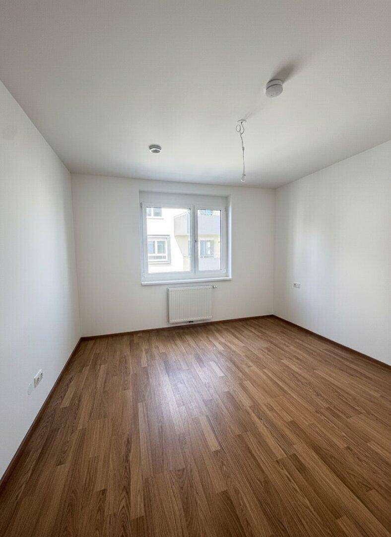 Unmöbliertes Zimmer mit Laminatboden, weiß gestrichenen Wänden und einem Fenster.