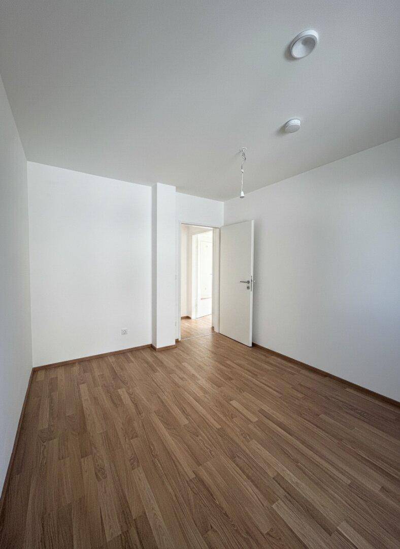 Leeres Zimmer mit Laminatboden und weißer Tür, ideal als Schlaf- oder Arbeitszimmer.