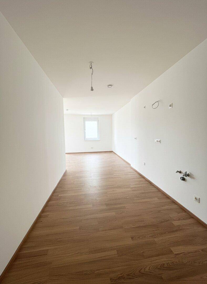 Leerer Küchenbereich mit Laminatboden und Anschlüssen für eine Einbauküche.