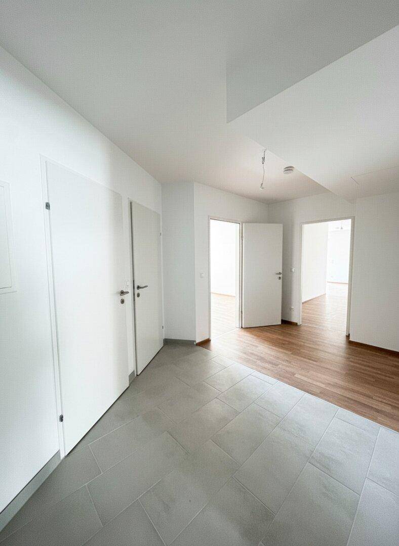 Heller Flur mit grauen Fliesen und Zugang zu mehreren Zimmern der Wohnung.