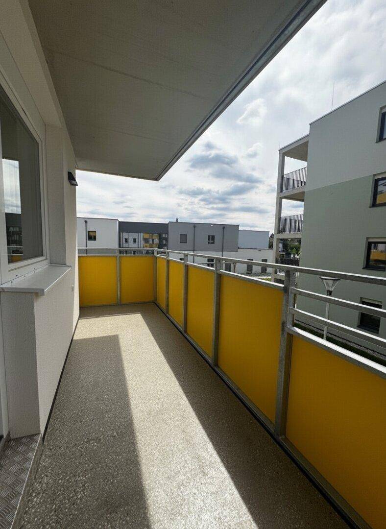 Geräumiger Balkon mit gelben Paneelen und Ausblick auf die Nachbarschaft.