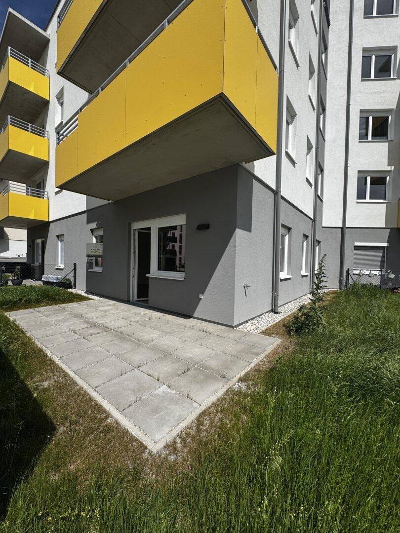 Erdgeschosswohnung mit privater Terrasse und Zugang zur Grünfläche eines modernen Gebäudes.