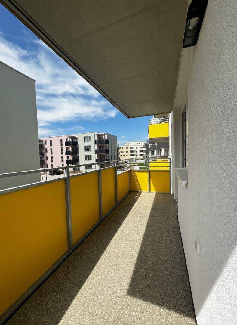 Langer Balkon mit gelben Sichtschutzelementen und Blick auf die umliegenden Neubauten.