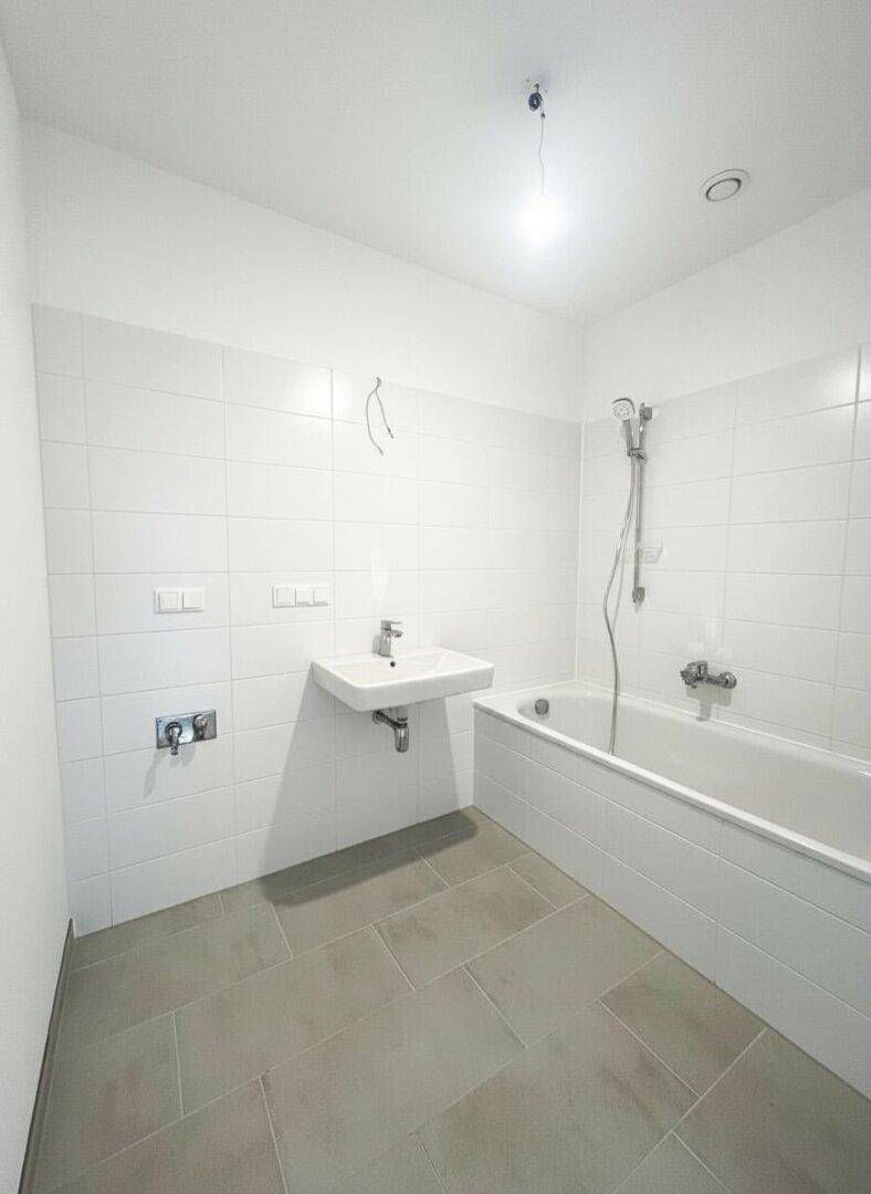 Modernes Badezimmer mit weißen Fliesen, Badewanne und Waschbecken.