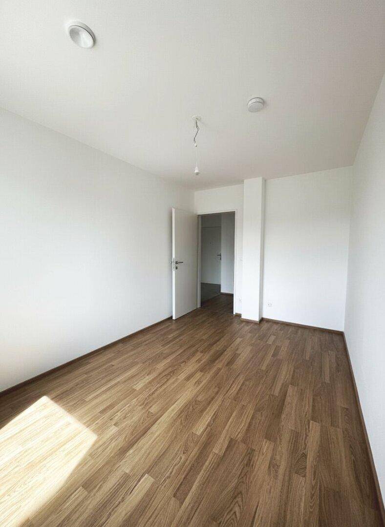 Leeres Schlafzimmer mit Laminatboden und weiß gestrichenen Wänden.