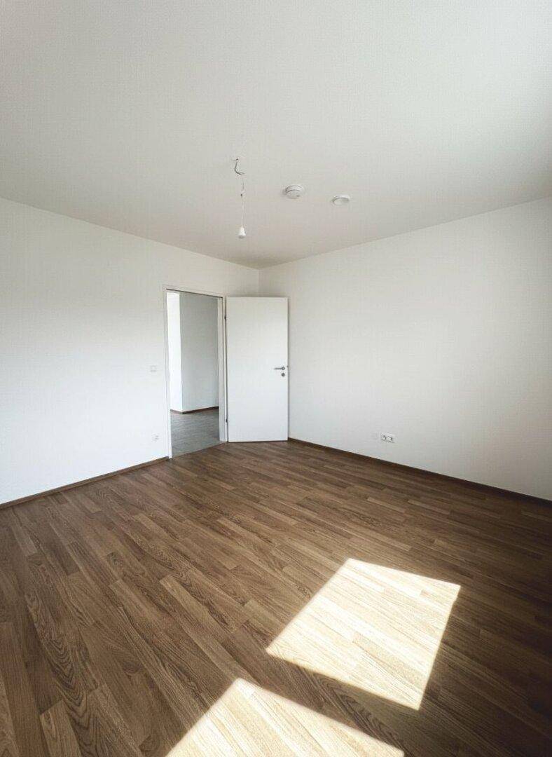 Heller Raum mit Laminatboden und offener Tür, bereit für die Einrichtung.