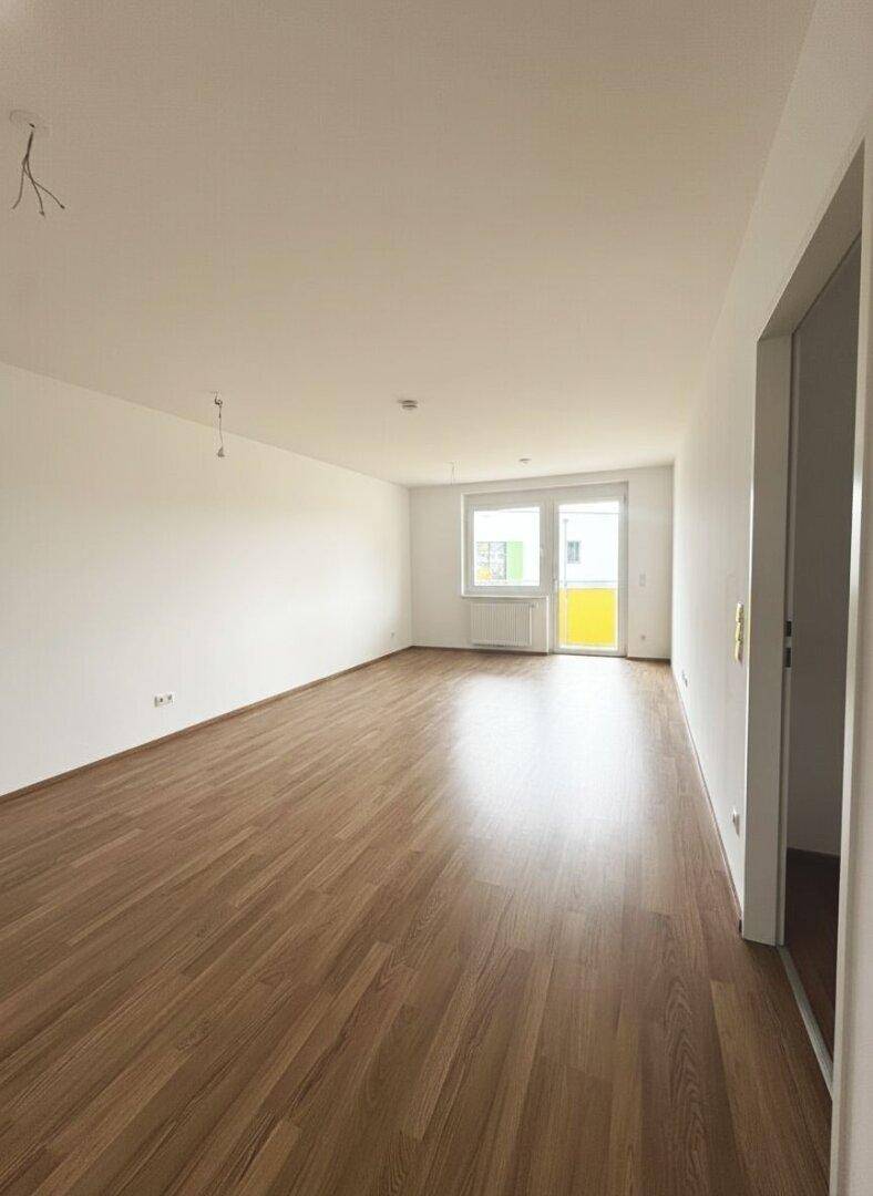 Geräumiges, leeres Wohnzimmer mit Laminatboden und Zugang zum sonnigen Balkon.