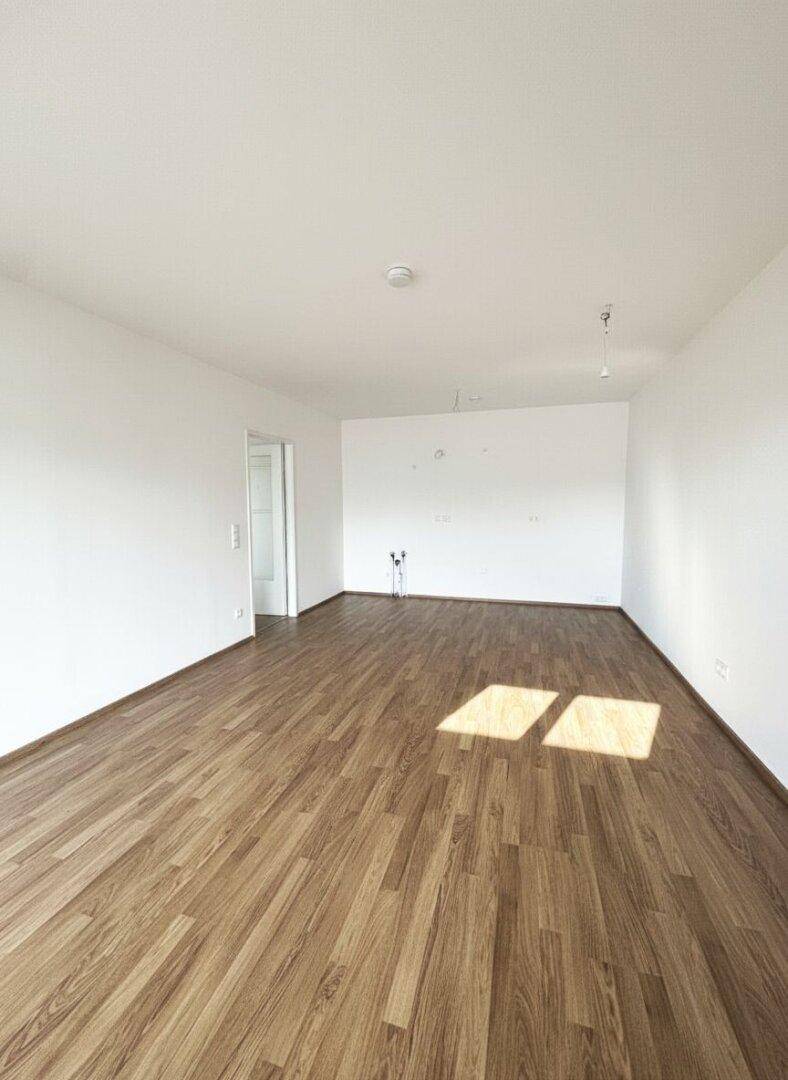 Geräumiges, unmöbliertes Wohnzimmer mit Laminatboden und viel Tageslicht.