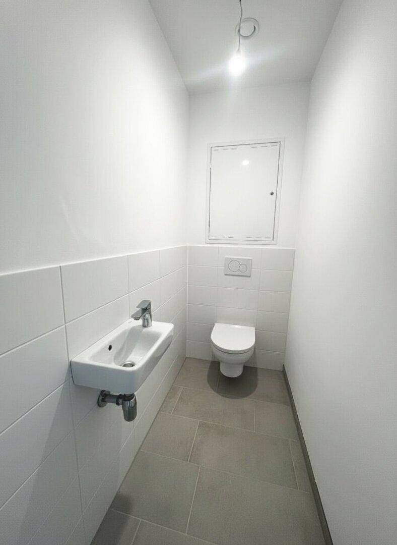 Kleines Gäste-WC mit wandhängendem WC, Waschbecken und hellgrauen Fliesen.