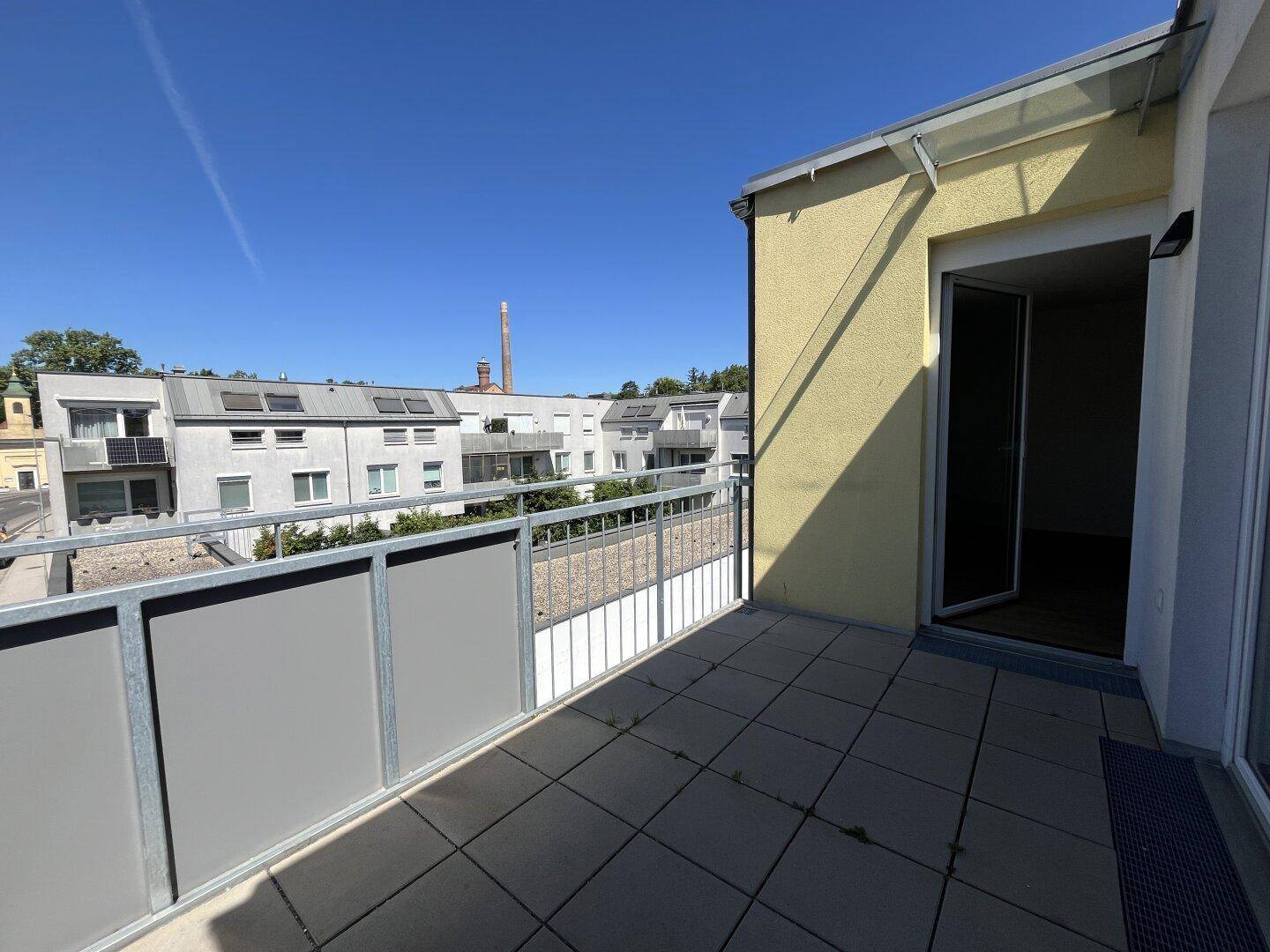 Sonniger Balkon mit Fliesenboden und Blick auf die umliegende Wohnbebauung unter blauem Himmel.