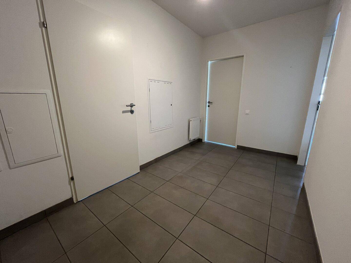 Geräumiger Flur mit grauen Fliesen und weißen Wänden, bietet einen klaren Eingangsbereich zur Wohnung.