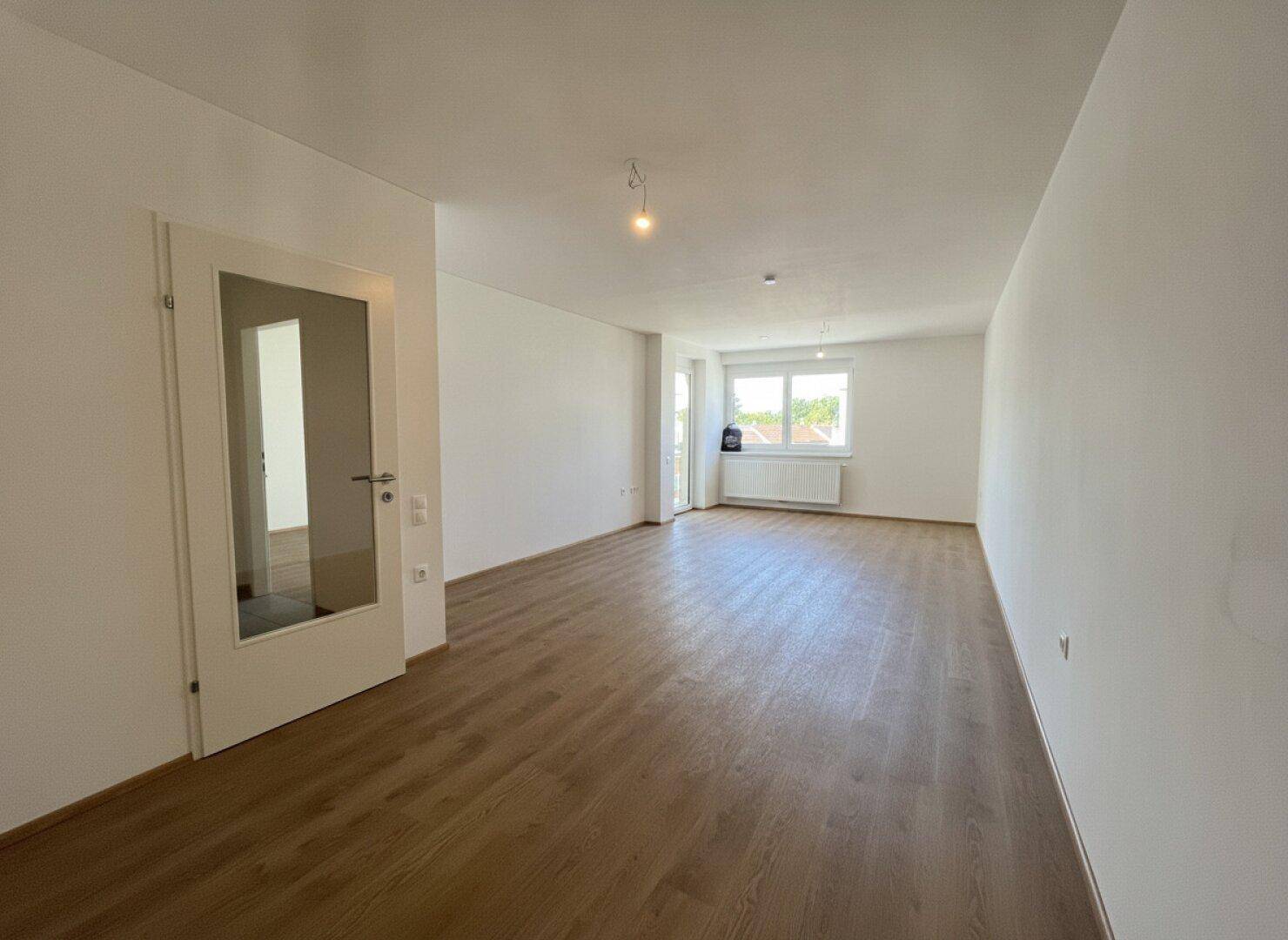 Heller, leerer Wohnraum mit neuem Laminatboden und weißen Wänden, bereit zur individuellen Gestaltung.
