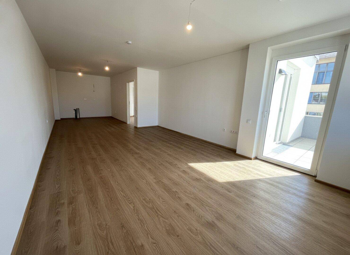 Großzügiger, heller Wohnbereich mit Laminatboden und Zugang zu einem Außenbereich, ideal für offenes Wohnen.