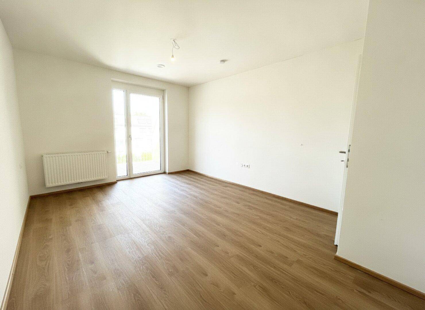 Helles Schlafzimmer mit Laminatboden, weißen Wänden und einem Fenster, das viel Tageslicht hereinlässt.