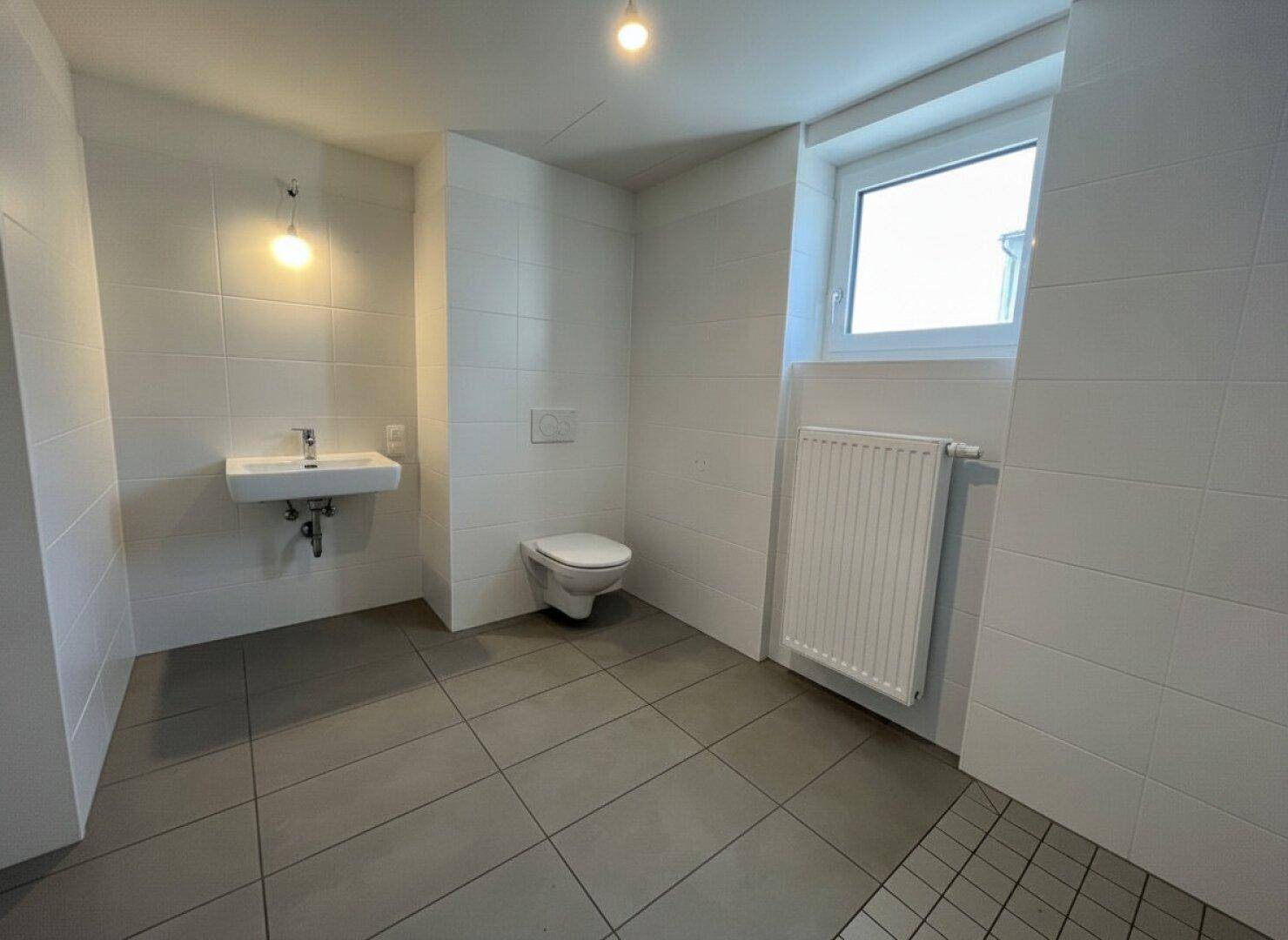 Helles Badezimmer mit modernen Fliesen, wandhängendem WC, Waschbecken und Fenster für natürliche Belüftung.