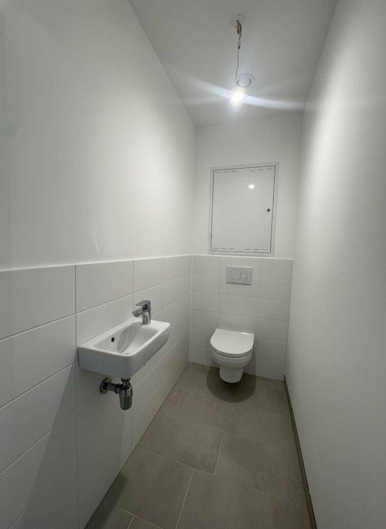 Separates Gäste-WC mit wandhängendem WC, kleinem Waschbecken und weißen Fliesen.