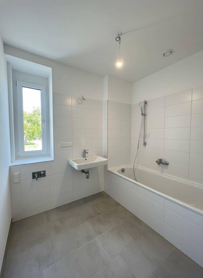 Modernes Badezimmer mit Badewanne, Waschbecken, weißen Fliesen und Fenster.