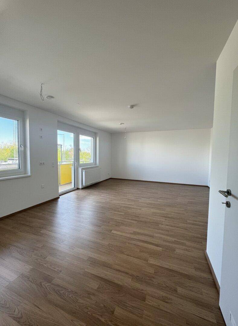 Geräumiges, unmöbliertes Wohnzimmer mit großen Fenstern und hellem Laminatboden.
