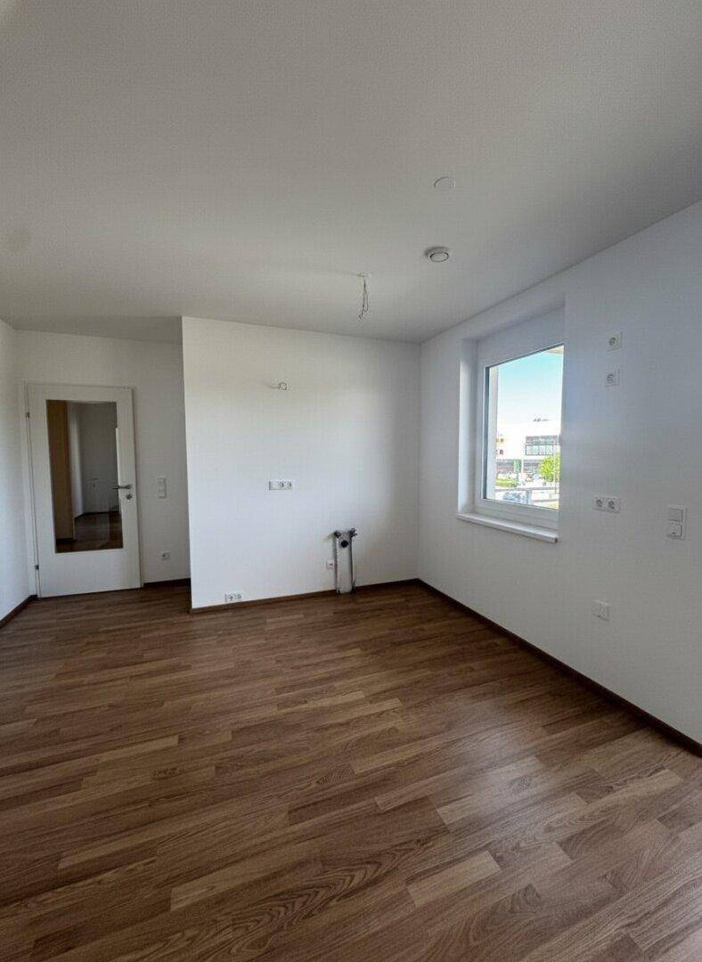 Heller Raum mit Laminatboden, weißen Wänden und Anschlussmöglichkeiten für eine Küche.