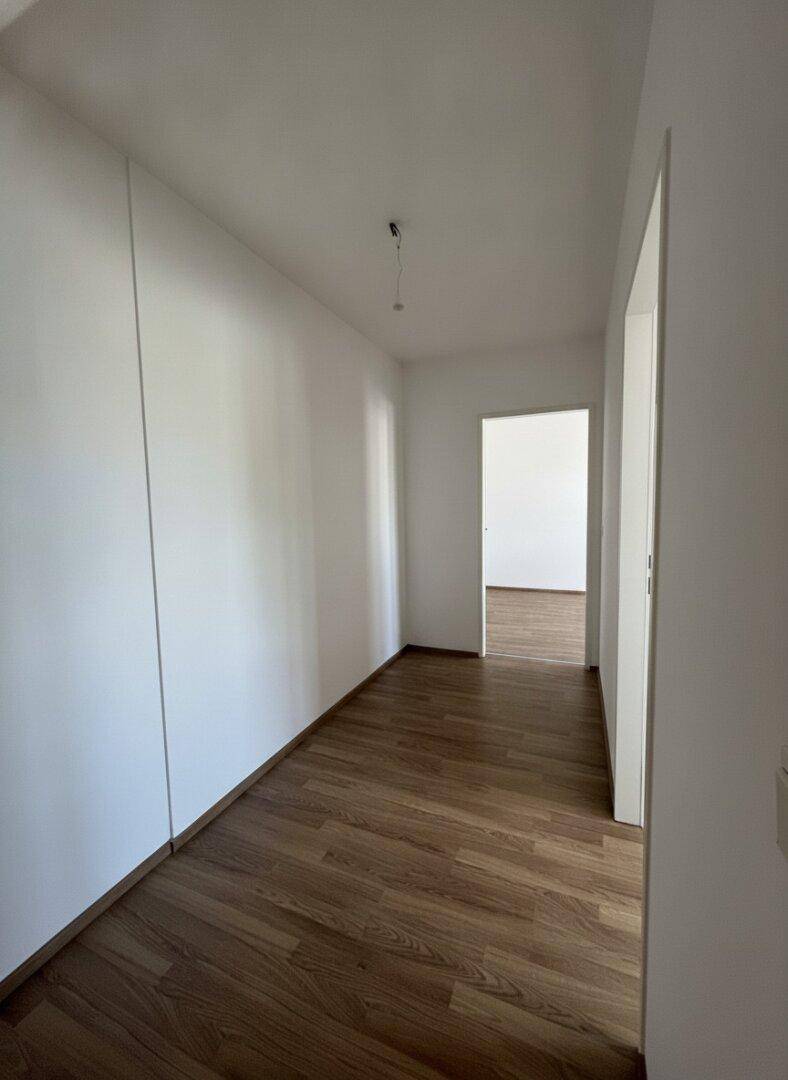 Heller Flur mit Laminatboden und weißen Wänden, der zu weiteren Räumen führt.