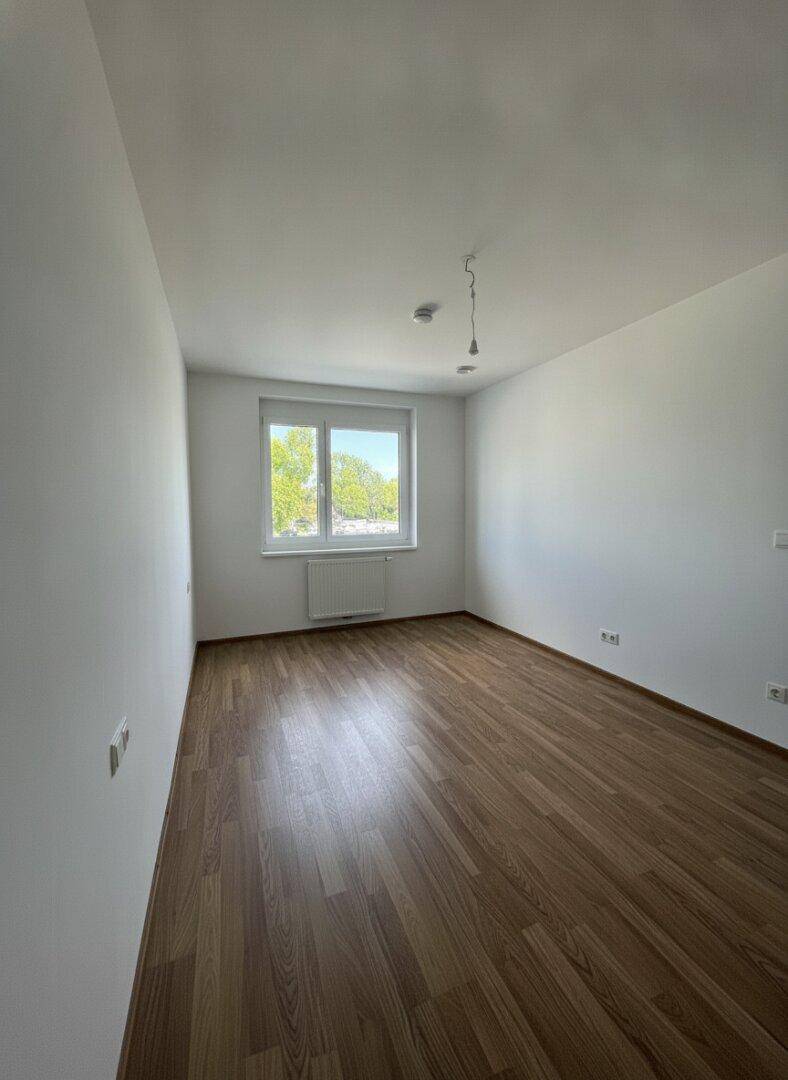Leeres Schlafzimmer mit Laminatboden, weiß gestrichenen Wänden und einem Fenster.