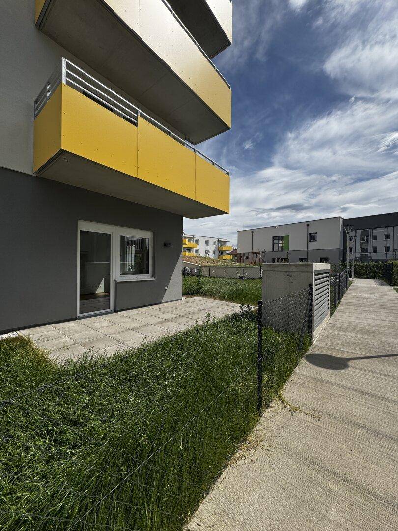 Moderne Wohnanlage mit gelben Balkonen und einer gepflasterten Terrasse im Erdgeschoss.