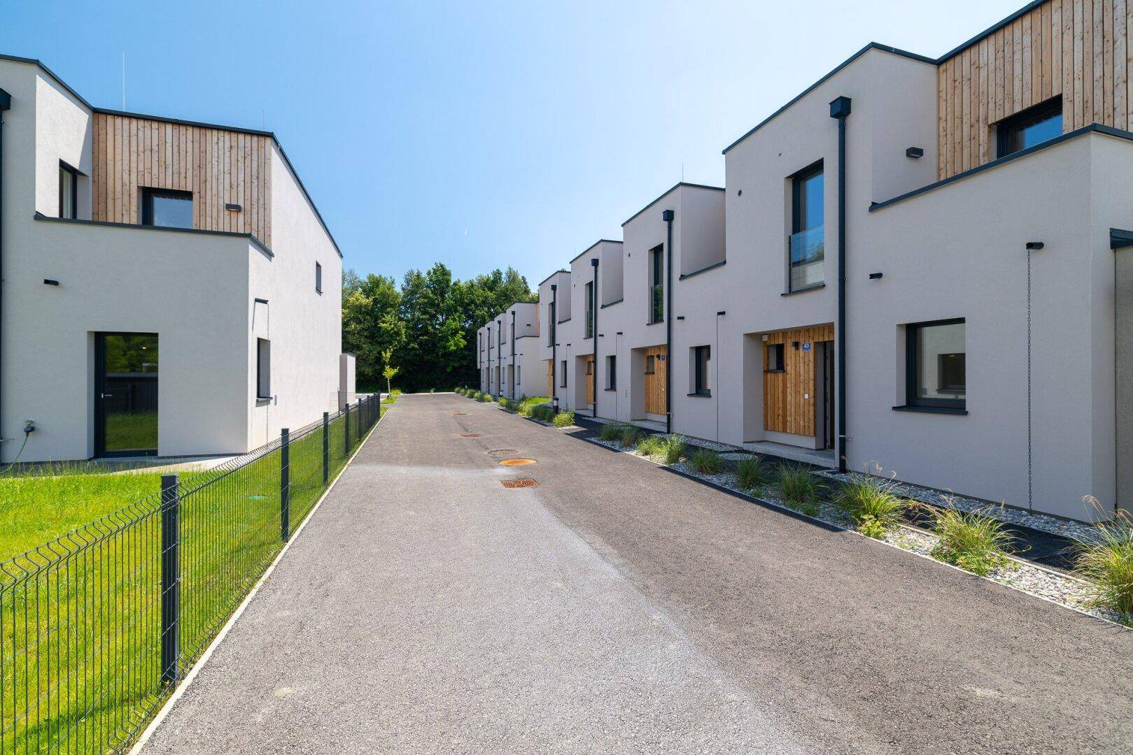 Gepflasterter Weg zwischen zwei Reihen moderner Häuser mit Holzakzenten und grünen Vorgärten.