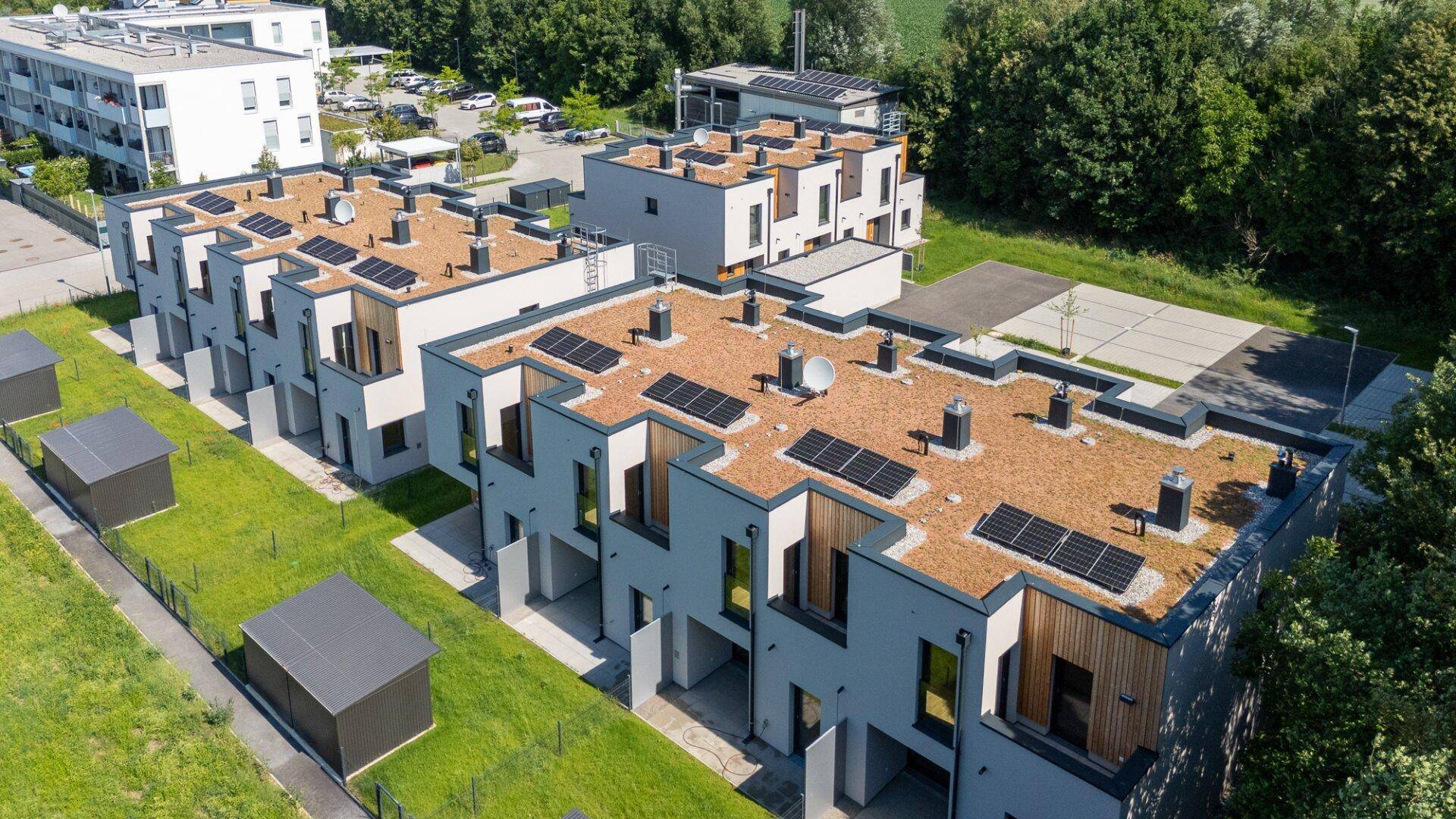 Überblick über die Reihenhaussiedlung mit Solarpaneelen auf den begrünten Dächern und umliegendem Grün.