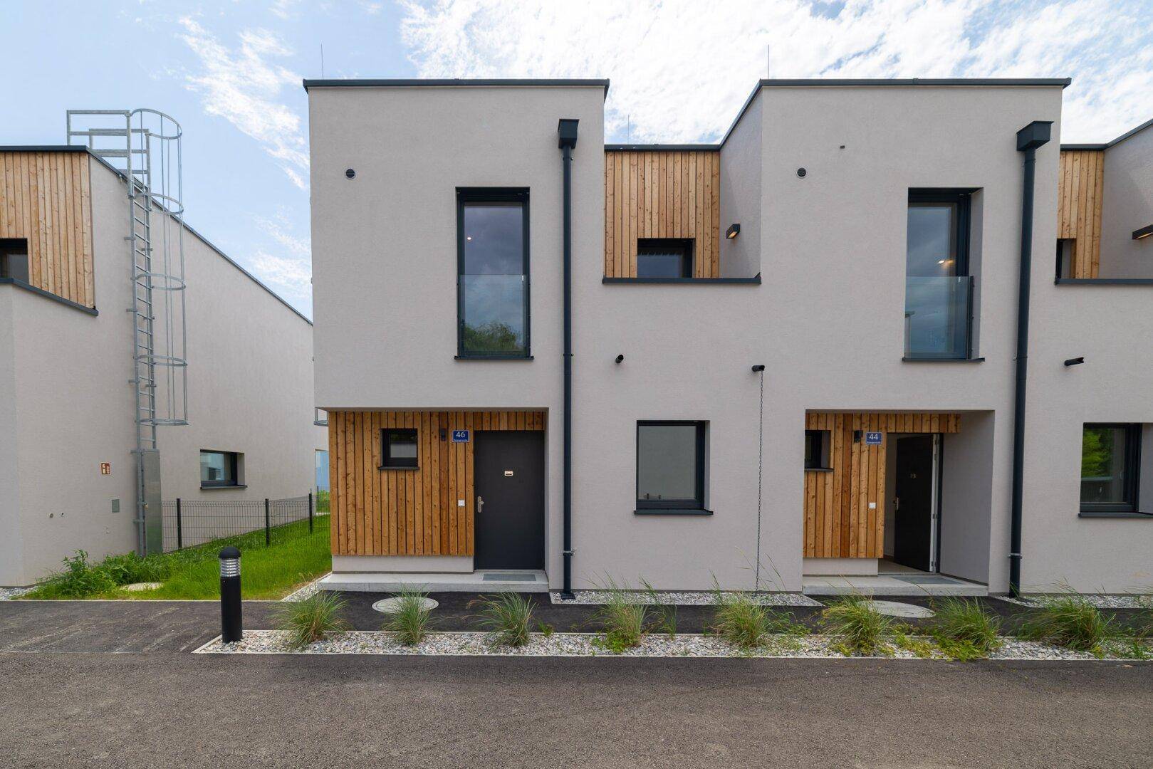 Moderne Reihenhäuser mit heller Fassade und Holzakzenten, umgeben von gepflegter Außenanlage.