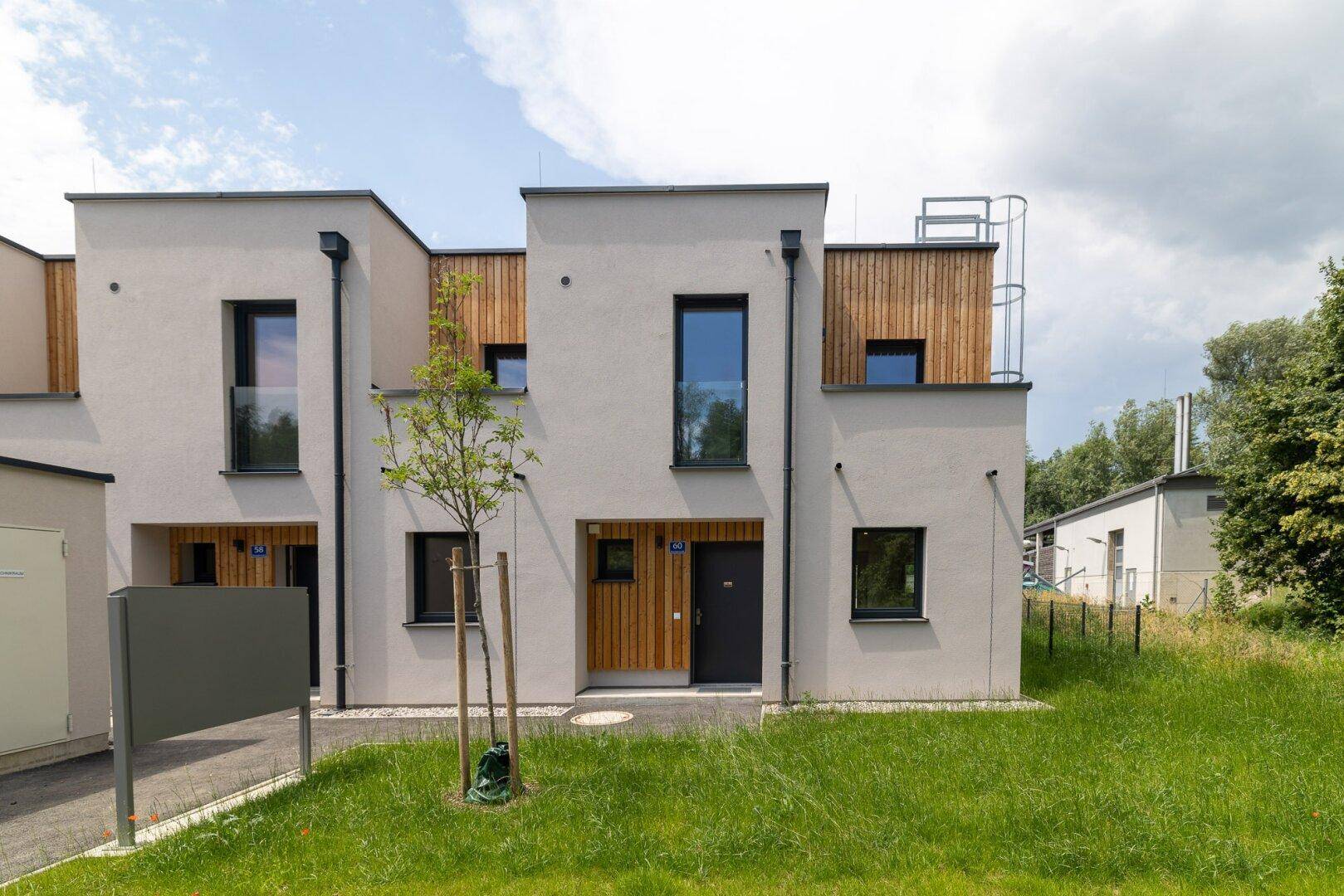 Neu gebaute Reihenhäuser mit moderner Architektur, hellen Fassaden und Holzelementen im Eingangsbereich.