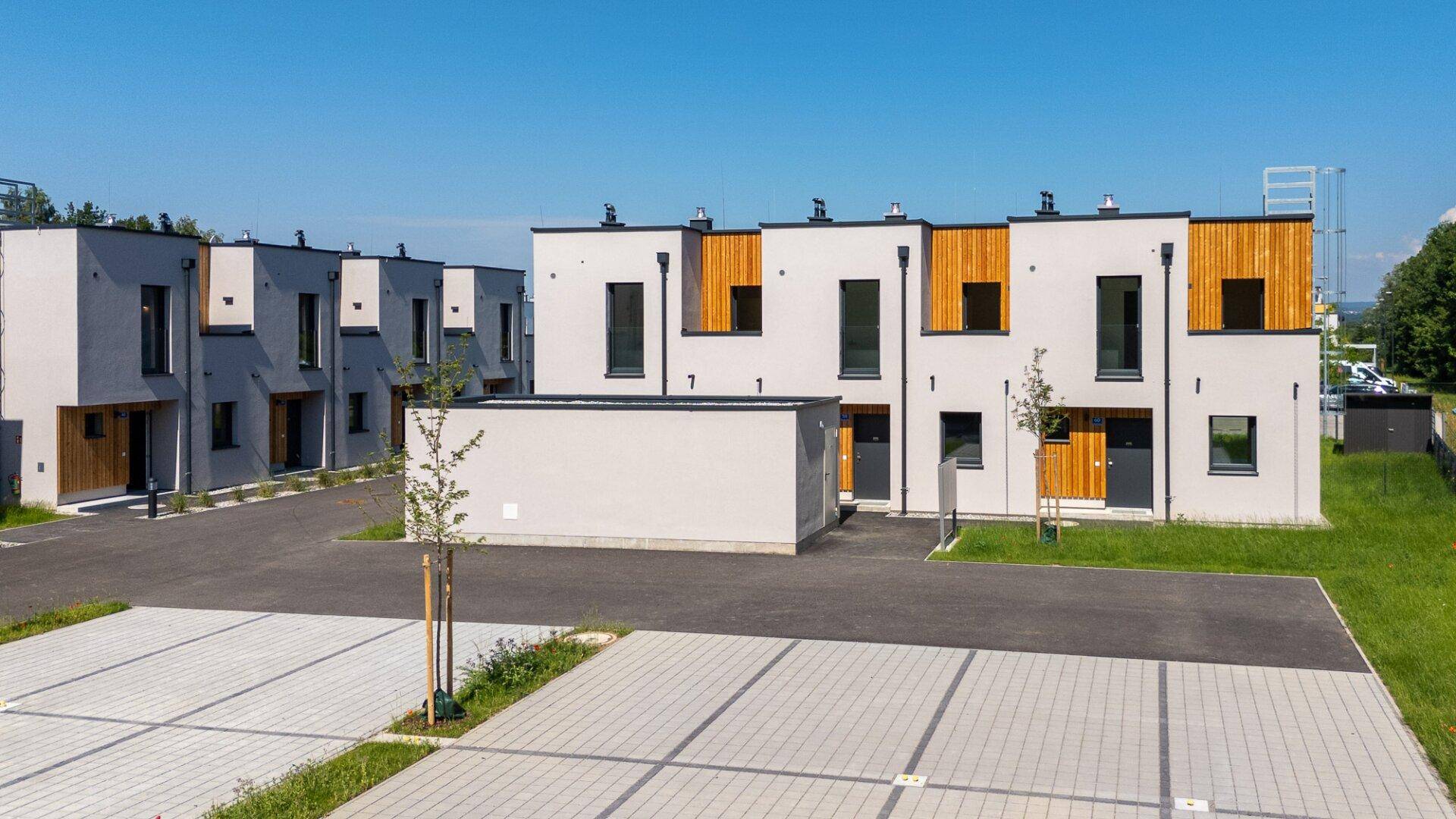 Überblick über eine Siedlung moderner Reihenhäuser mit Parkplätzen und Grünflächen unter blauem Himmel.