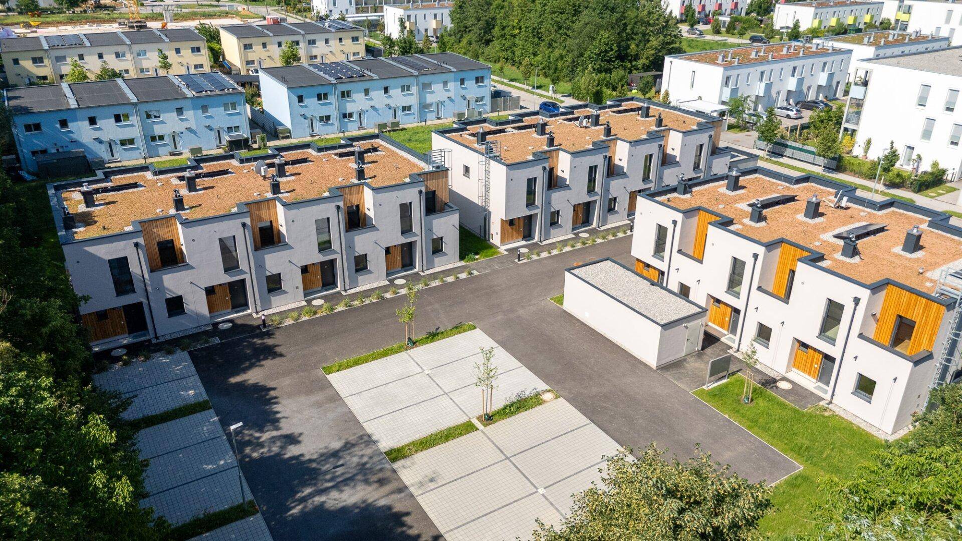 Weitläufige Luftaufnahme einer modernen Wohnsiedlung mit Reihenhäusern, Parkplätzen und angrenzenden Gebäuden.