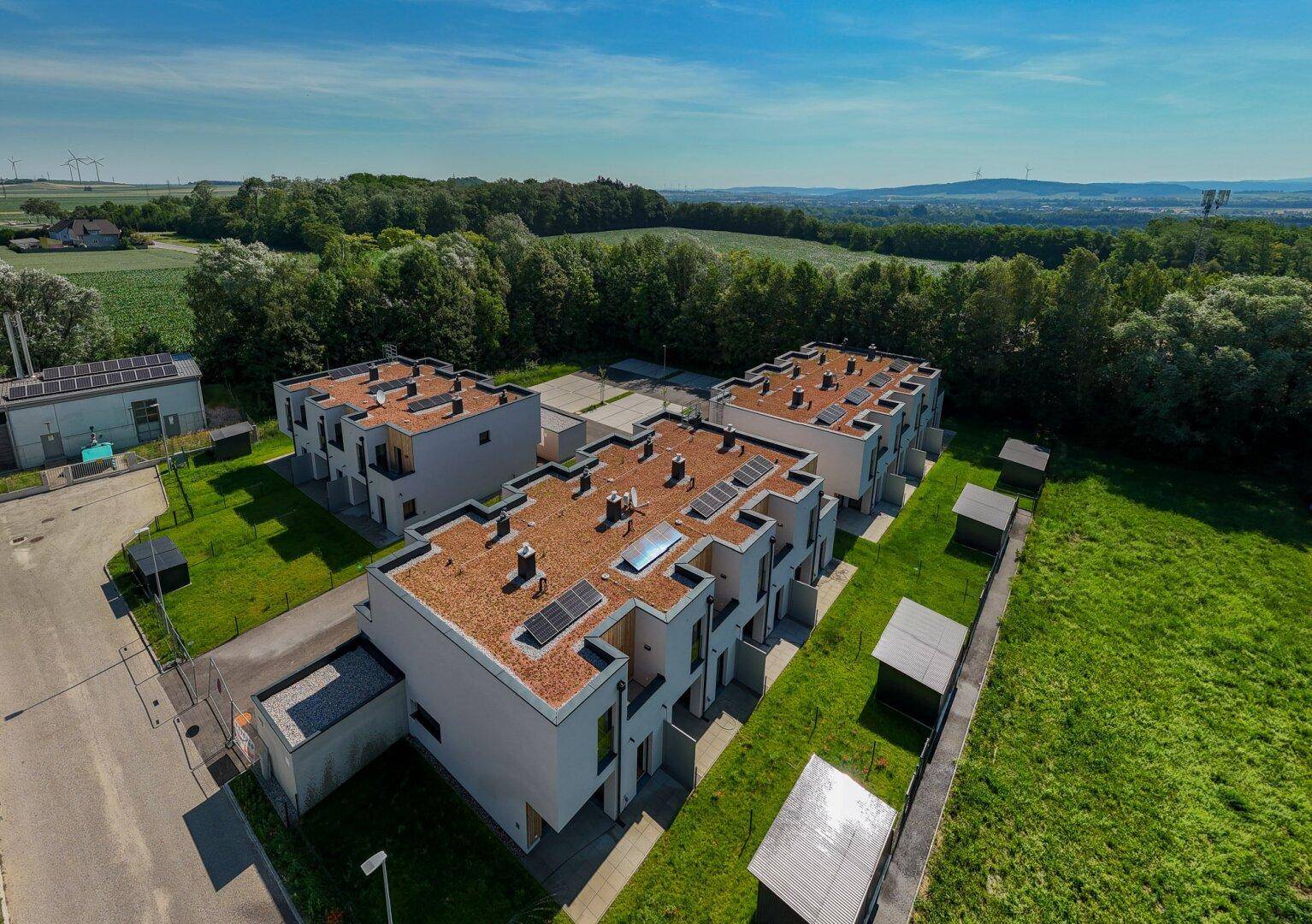 Panoramablick auf eine moderne Reihenhaussiedlung mit Photovoltaikanlagen, umgeben von weiten Grünflächen und Landschaft.