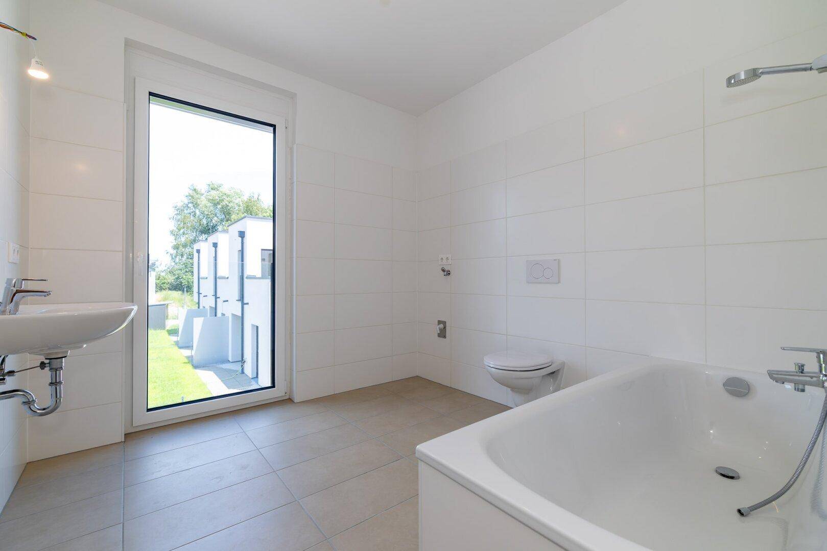 Modernes Badezimmer mit Badewanne, WC, Waschbecken und großem Fenster für natürliches Licht.