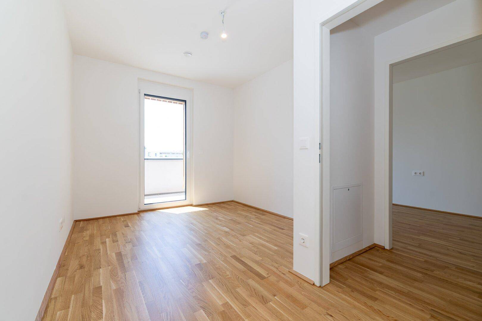Helles Schlafzimmer mit Eichenparkettboden und Zugang zu einem Balkon, ideal für Entspannung.