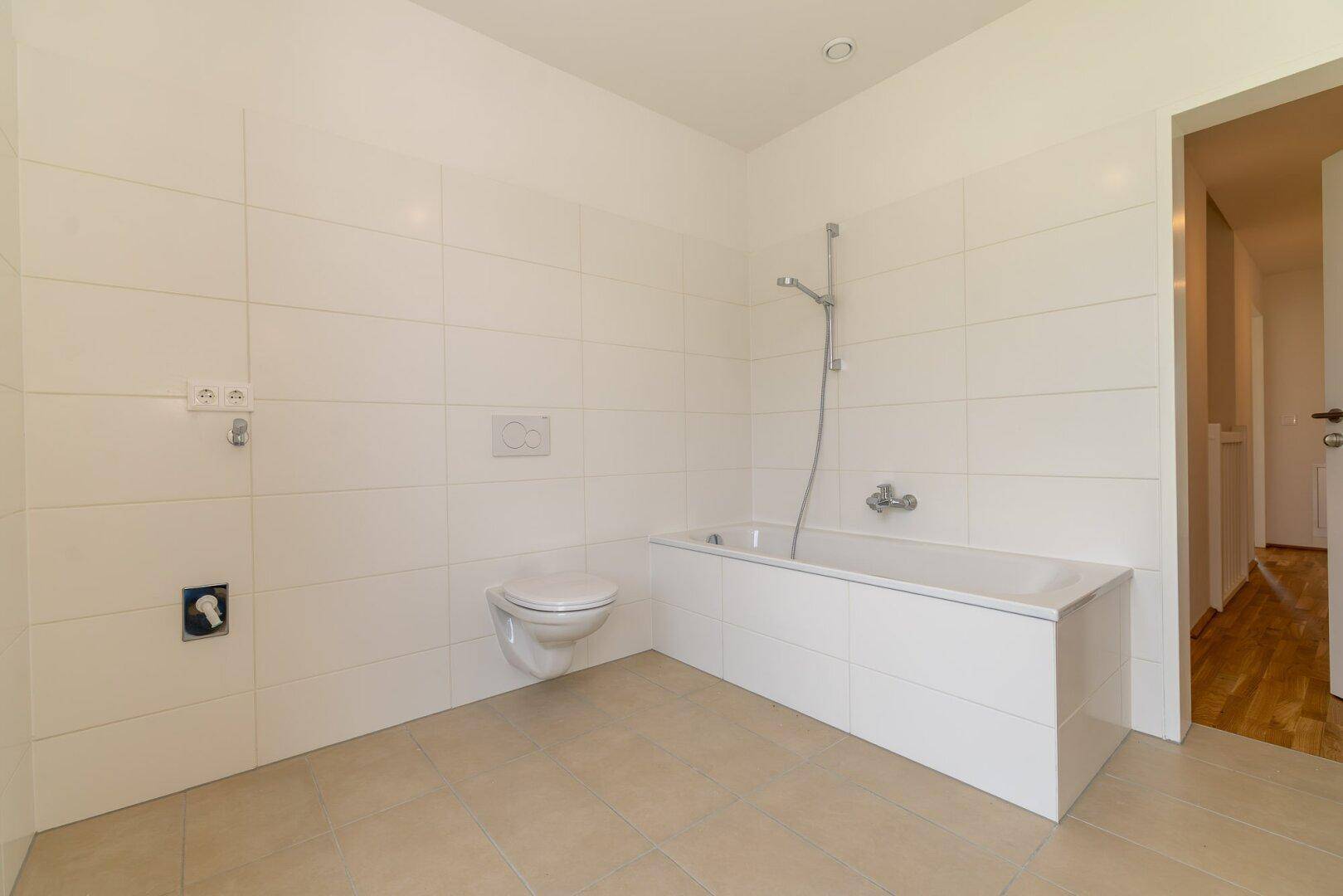Modernes Badezimmer mit weißen Fliesen, Badewanne und wandhängendem WC in neuwertigem Zustand.