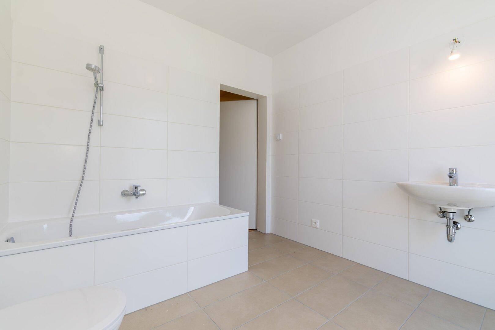 Helles Badezimmer mit weißen Fliesen, Badewanne, WC und Waschbecken in minimalistischem Design.