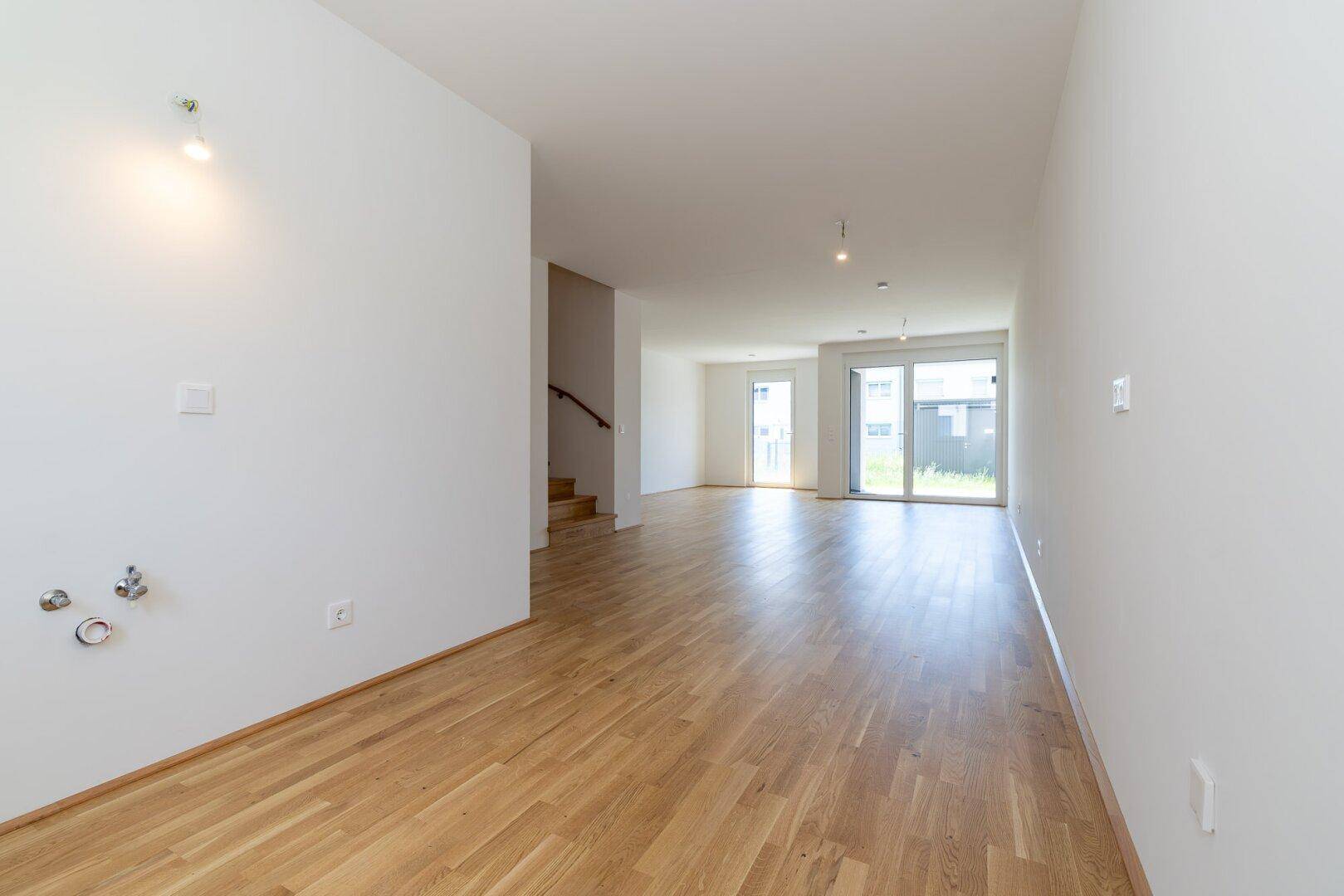 Geräumiger, unmöblierter Wohnbereich mit Holzparkett und Treppenaufgang in die obere Etage.