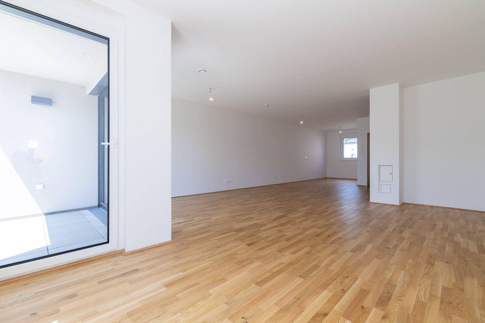 Heller Wohnbereich mit Parkettboden und großem Fenster, das viel natürliches Licht hereinlässt.
