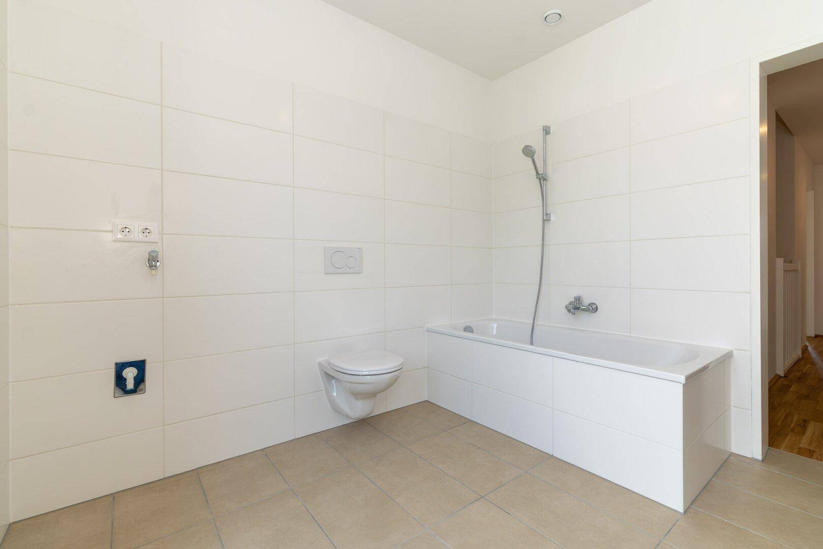 Modernes Badezimmer mit weißen Fliesen, Badewanne und wandhängendem WC, bereit zur Nutzung.